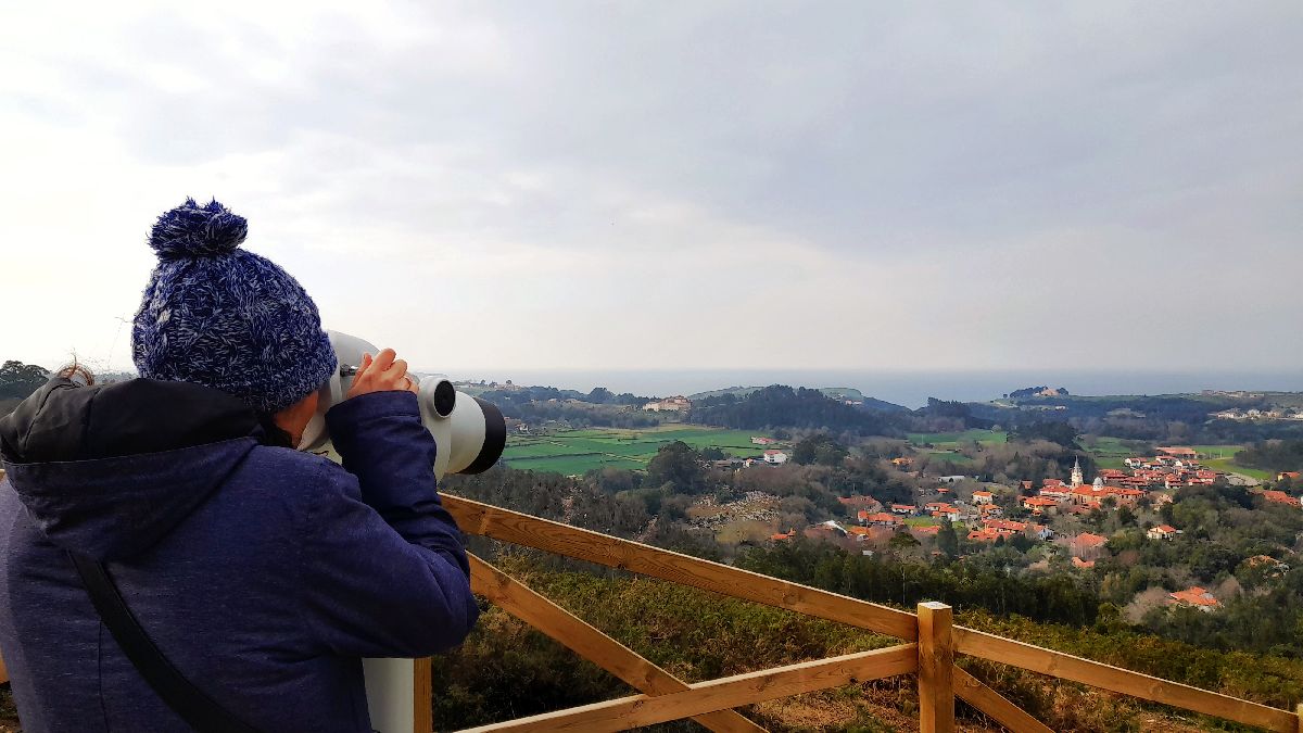 Mujer mirando por telescopio. Vista del Barrio de La Iglesia con el mar Cantábrico de fondo