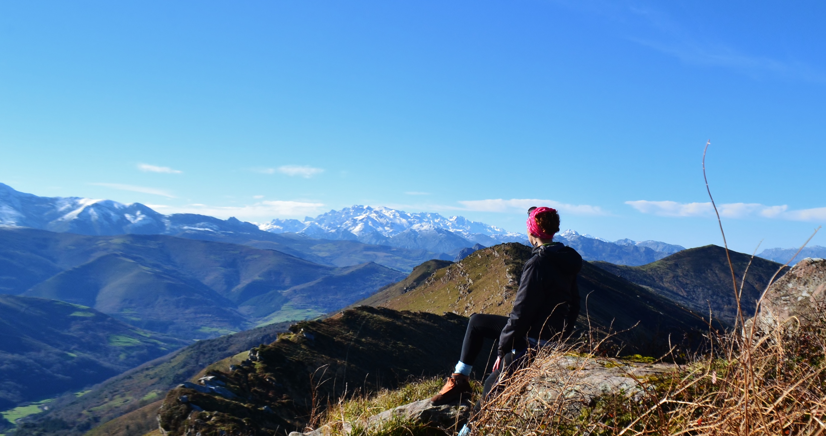 Mujer en la cumbre de la Sierra del Escudo de Cabuérniga. La vista es la Sierra de peña Sagra y los Picos de Europa nevados